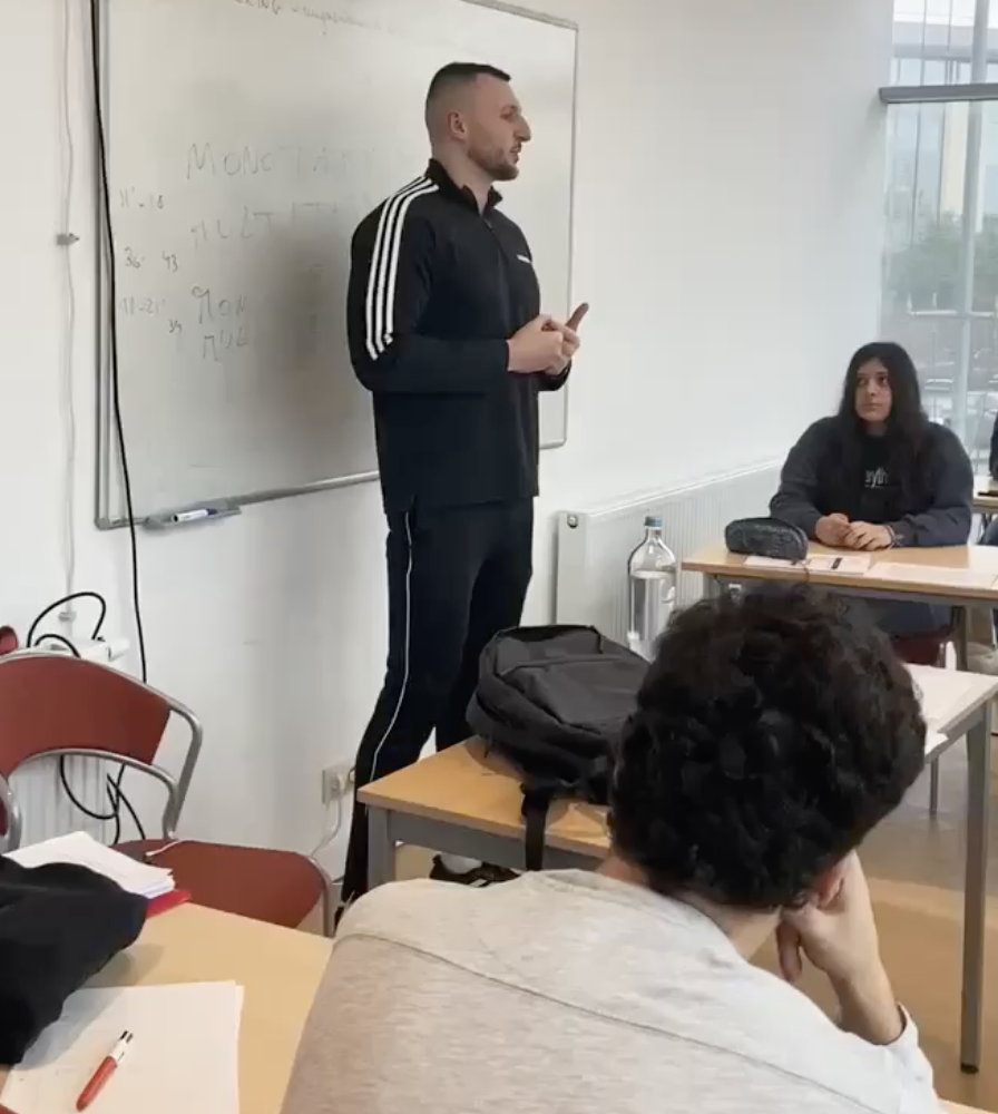 Un intervenant debout devant un tableau blanc parle aux élèves dans une salle de classe.